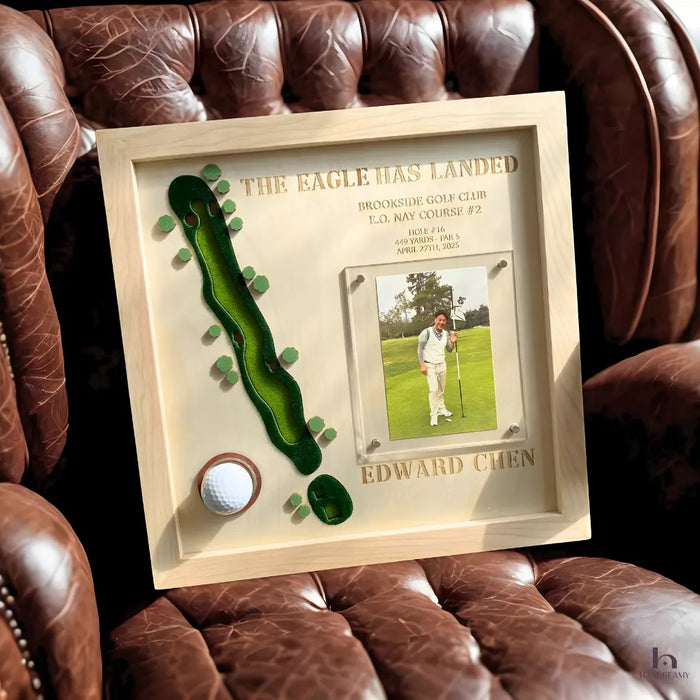 Framed golf-themed artwork with a golf ball and photo of a golfer on a brown leather couch.