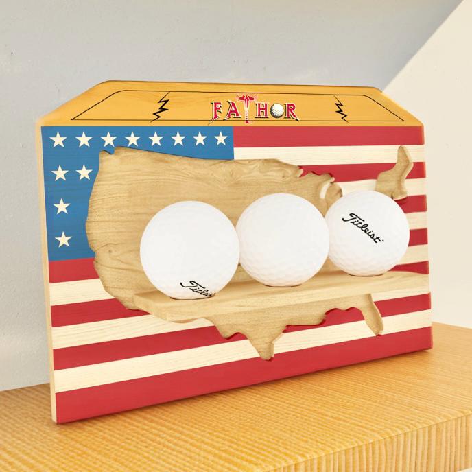 Three golf balls in a wooden holder with an American flag design on a box labeled 'FATHOR'.