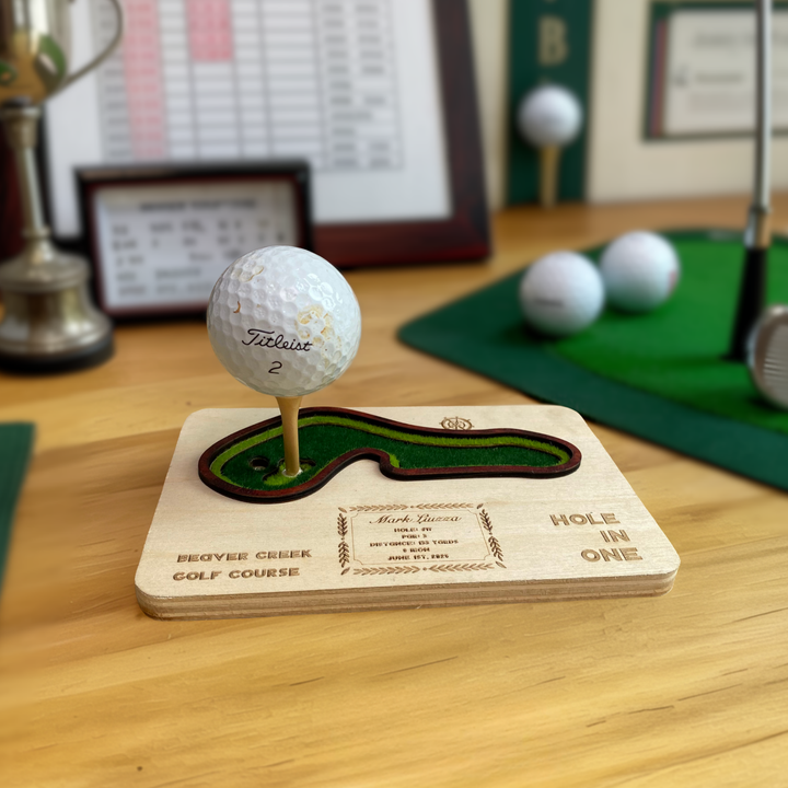 Golf ball on a tee with a wooden plaque at a golf course, surrounded by golfing equipment and memorabilia.