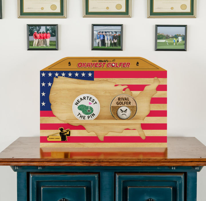 Wooden box with golf-themed designs and text on a table against a wall with framed pictures.