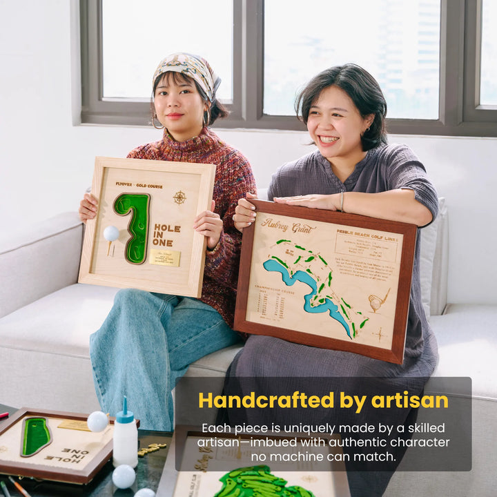 Two women holding framed wooden art pieces in a bright room.