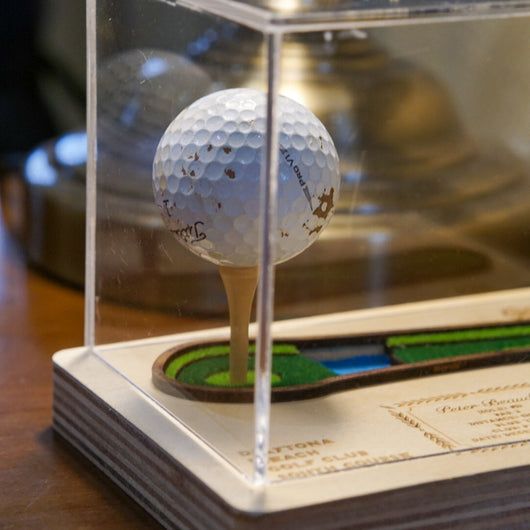 Golf ball on a tee in a clear display case with a blurred background