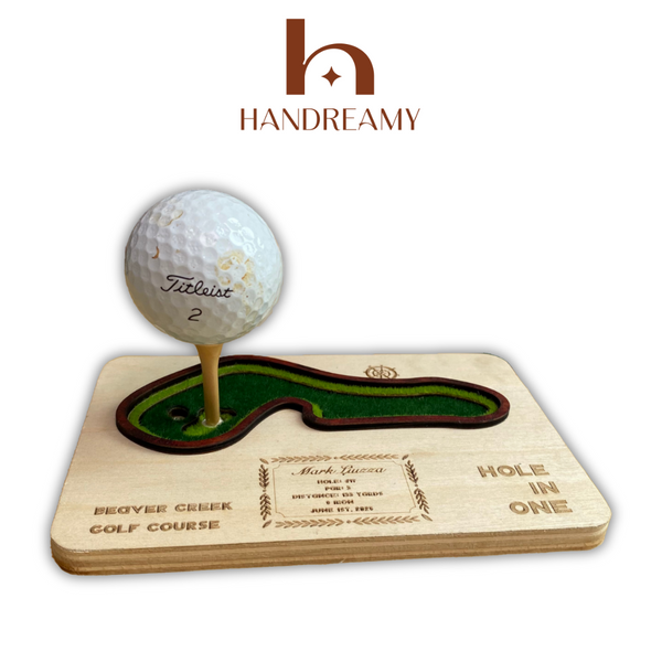 Golf ball on a wooden tee with a golf course design, featuring the Handreamy brand.
