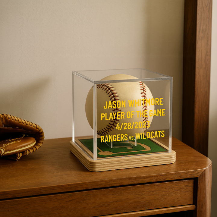 Baseball in a clear display case on a wooden surface with a glove beside it.